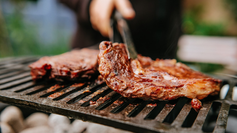 tongs holding a piece of beef on a charcoal grill