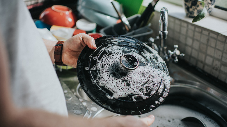 A man cleaning the lid of a black Dutch oven in the sink