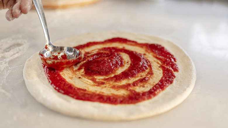 Hand ladling tomato sauce on round of pizza dough