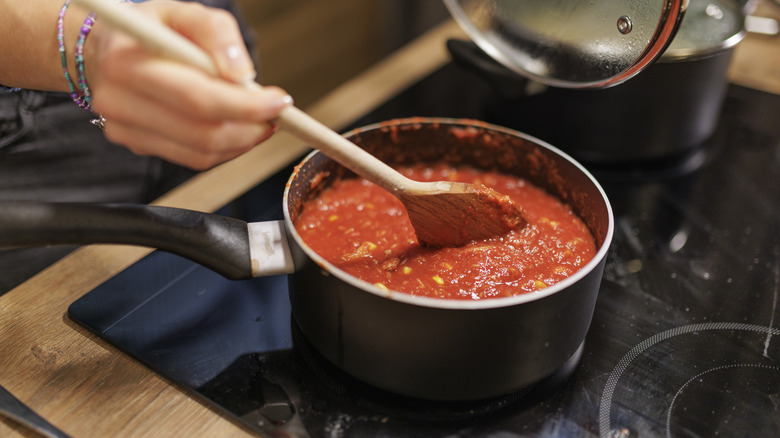 a woman stirring a pot of red sauce