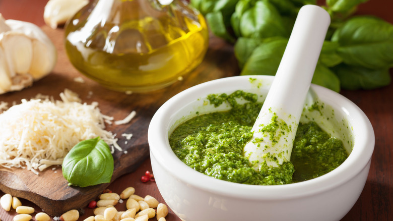 Basil pesto in a white mortar and pestal with pesto ingredients roundabout