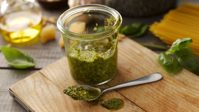 A glass jar and a spoonful of homemade pesto on a wooden chopping board