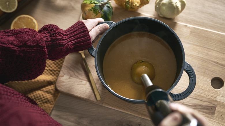 person blending soup with immersion blender