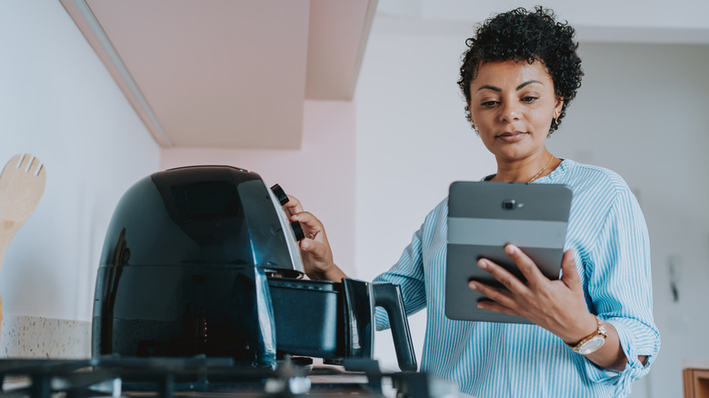 Woman preparing food in an air fryer while reading from and tablet