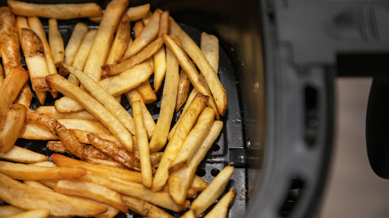 French fries sit in a black air fryer basket on a counter