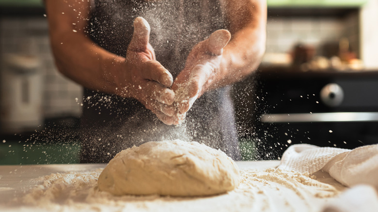 A person kneading bread dough on a wooden table.