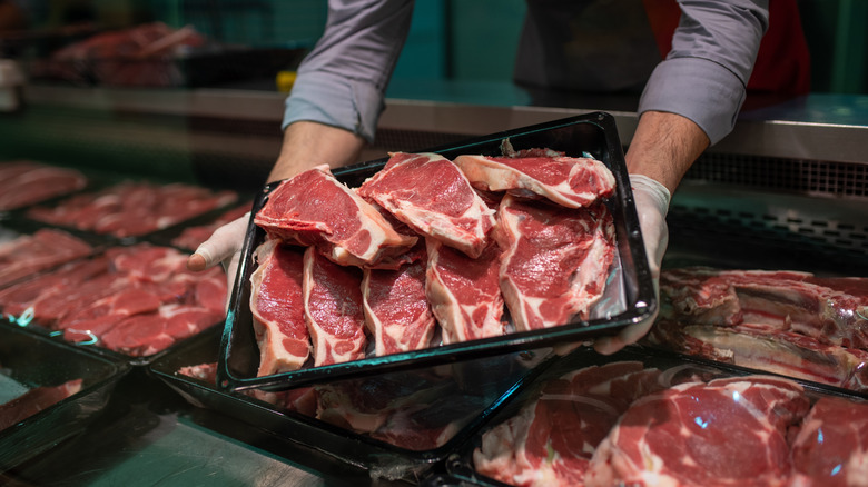 A person holding a tray of meat at a grocery store.