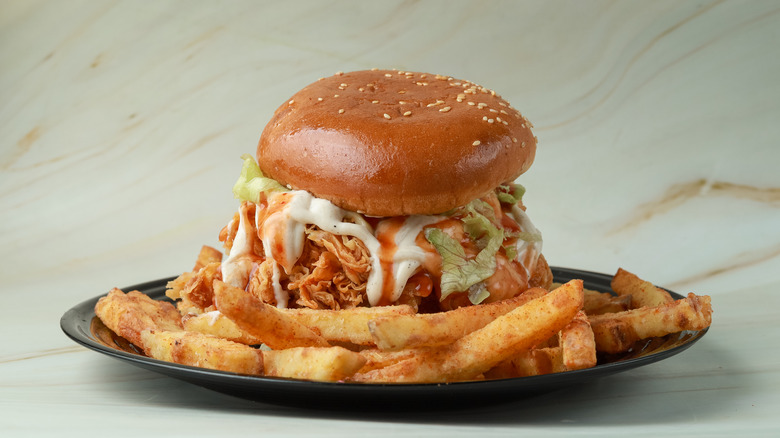 A burger with a side of crispy fries and mayonnaise dripping out.