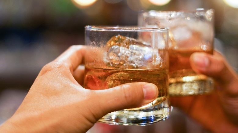 Two hands holding glasses of bourbon on the rocks