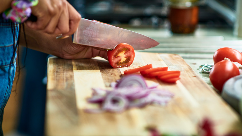 Person using a sharp kitchen knife to slice tomatoes on a cutting board