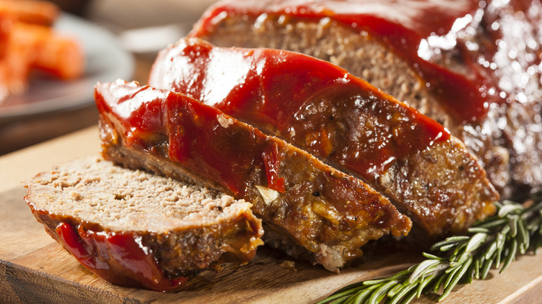 A beautifully sliced meatloaf on a wooden cutting board garnished with rosemary and BBQ sauce