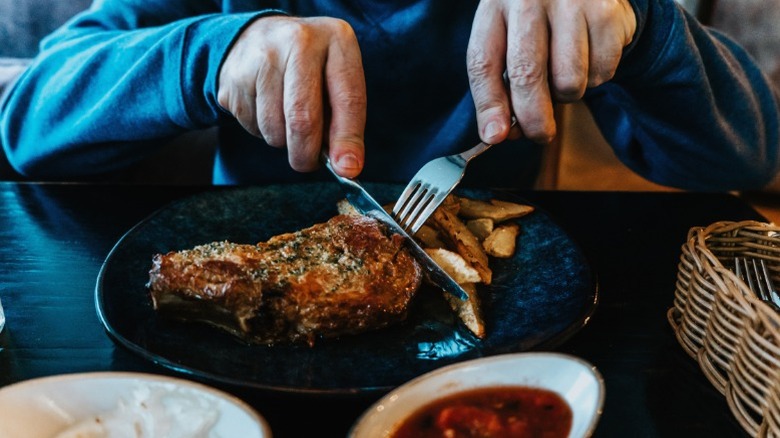 A man cutting his steak at a restaurant.