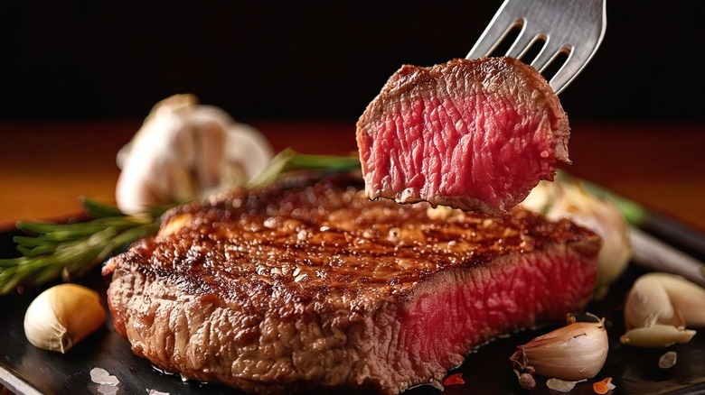 A juicy rare steak with one piece shown off on a fork.