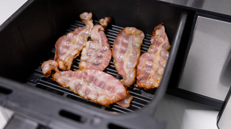 five pieces of bacon cooking on the inside of an air fryer