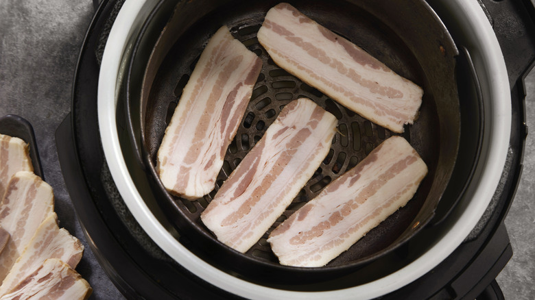 four pieces of uncooked bacon inside an air fryer