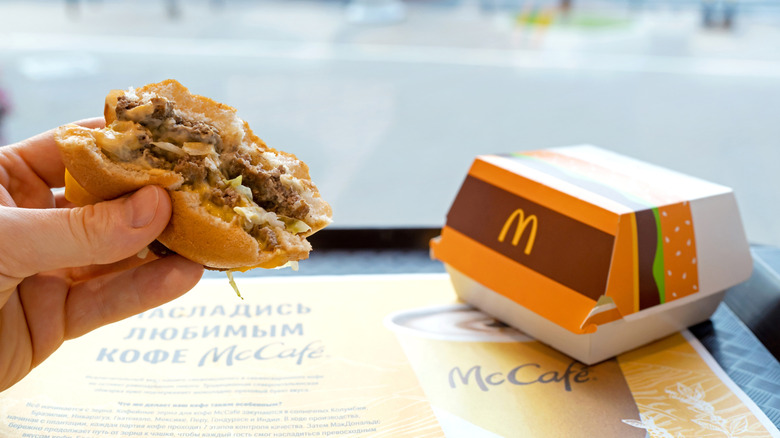 A hand gripping a half-eaten McDonald's burger with the box it came in nearby.