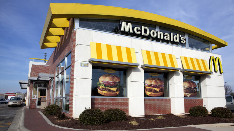 A photo of the outside of a McDonald's and a drive through with a gold car waiting to pick up food.