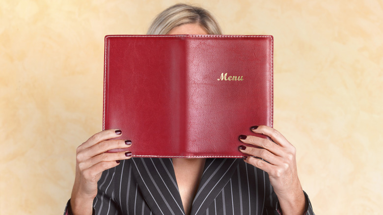 Blonde woman holding a red menu in front of her face