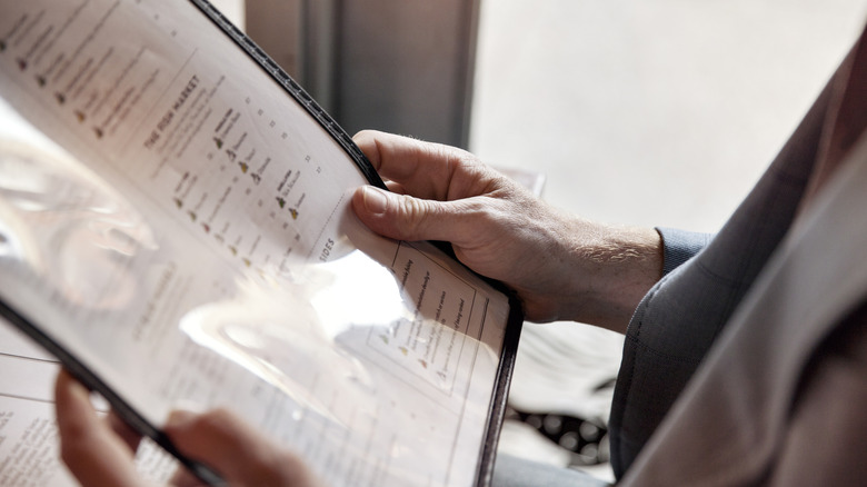 A man holding an unreadable restaurant menu while sitting down