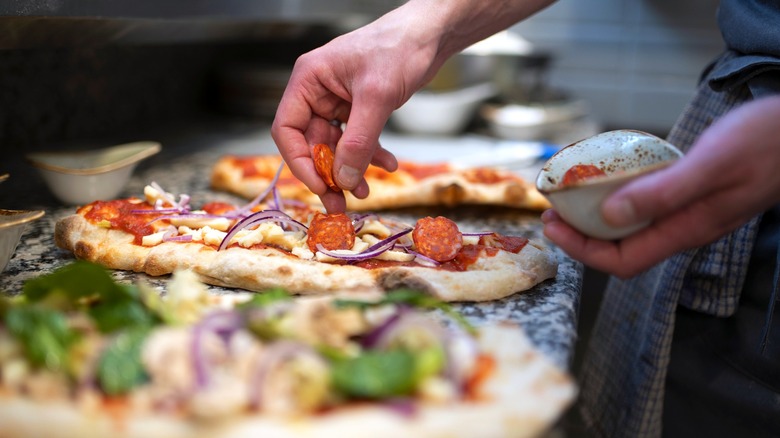 A pizza shop worker puts pepperoni on a pizza