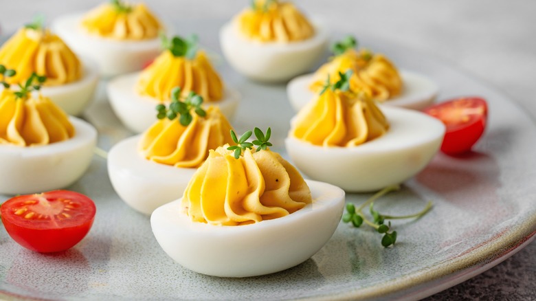 Deviled eggs on a plate with cherry tomatoes and a herb garnish