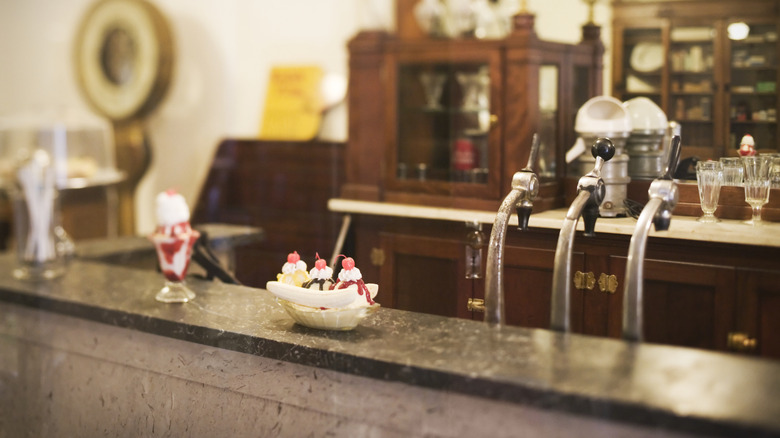 A bar with a soda fountain and a banana split dessert topped with ice cream sitting on it