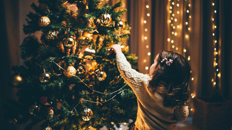 little girl putting ornaments on Christmas tree