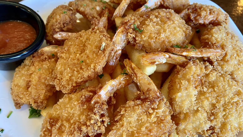 Fried shrimp on a white plate with a small black bowl of cocktail sauce