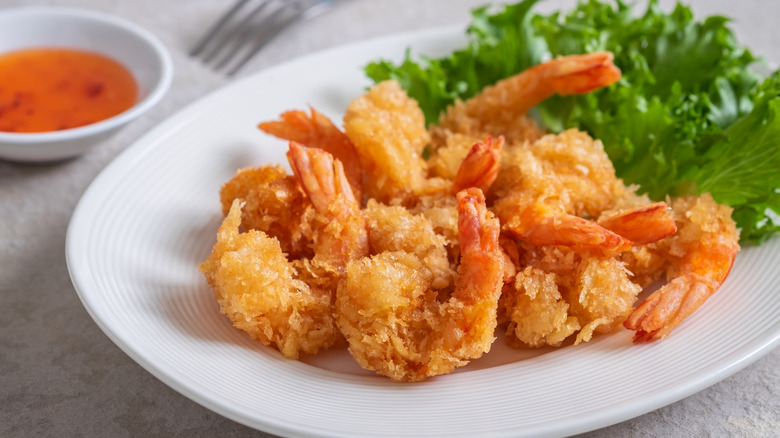 Fried shrimp on a white plate with a small bowl of sauce