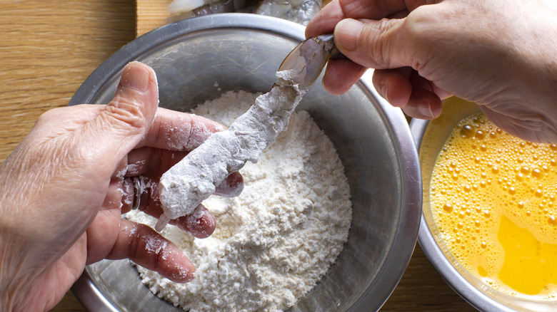 Person's hands dipping raw shrimp in flour