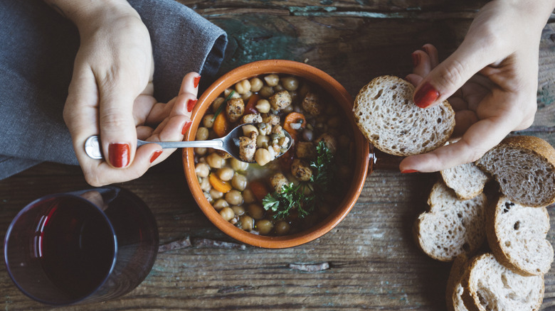 woman's hands scoop bean soup with bread