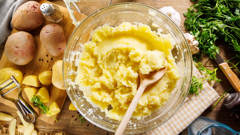 mashed potatoes in a clear bowl surrounded by raw potatoes