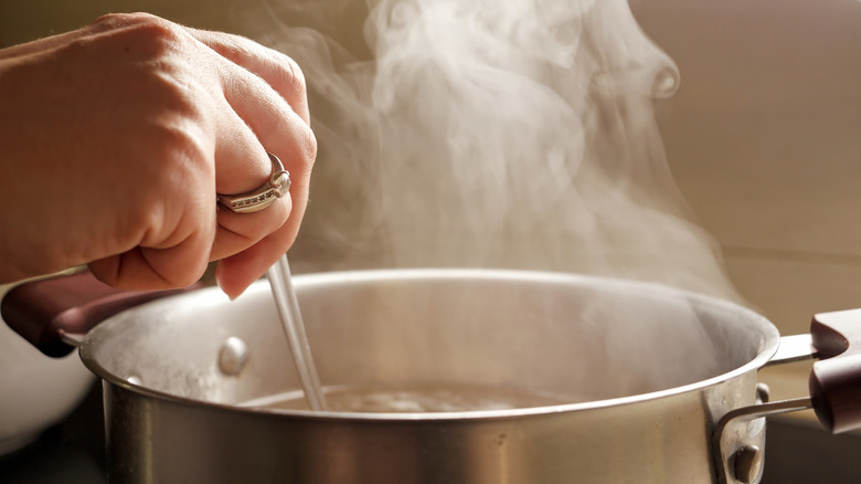 A hand stirring a steaming pot of liquid