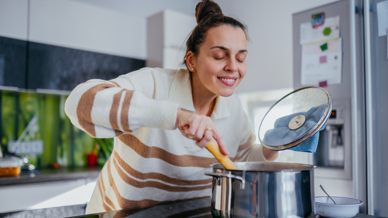 A person lifting the lid off of a pot to stir and smell its contents