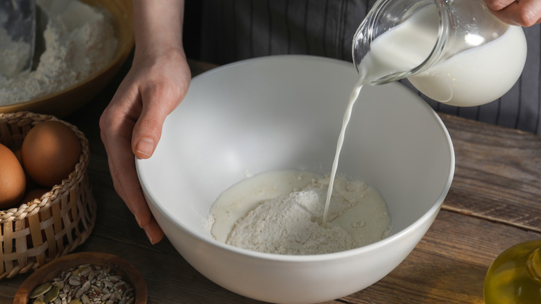 A hand pours milk into a bowl with flour