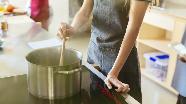 A person standing over a steaming pot on the stove and stirring