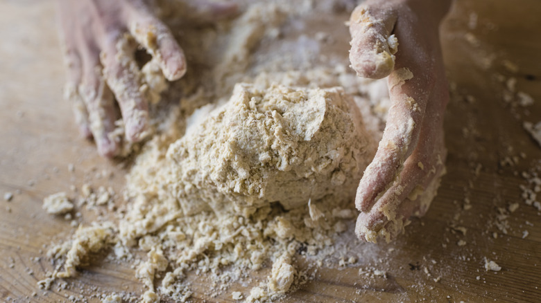 Hands pushing crumbly dough together on a wooden surface