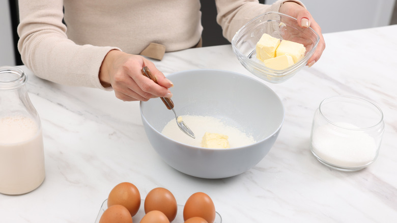 Person adding butter to flour in a white bowl