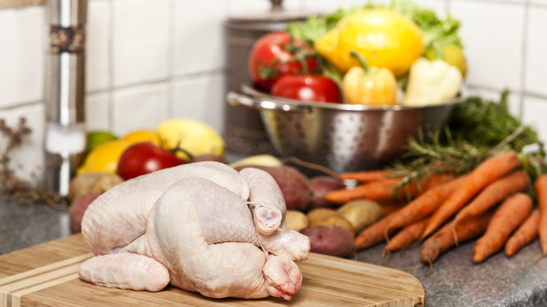 A raw whole chicken and vegetables on a kitchen counter