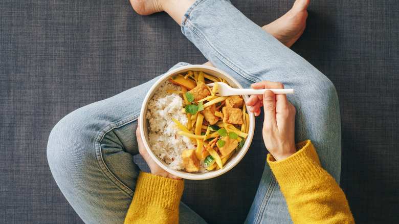 Person sitting and eating tofu with rice