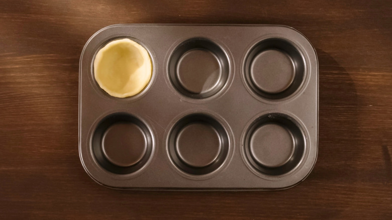 A muffin tin with cookie dough pressed down in one mold