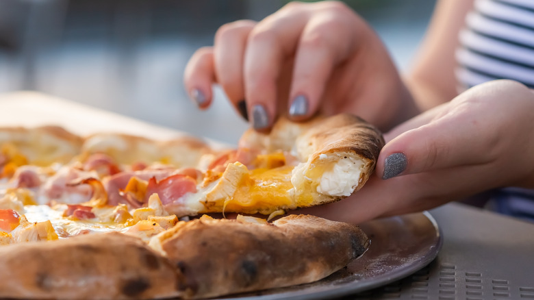 A person's hand taking a slide of cheese stuffed crust pizza