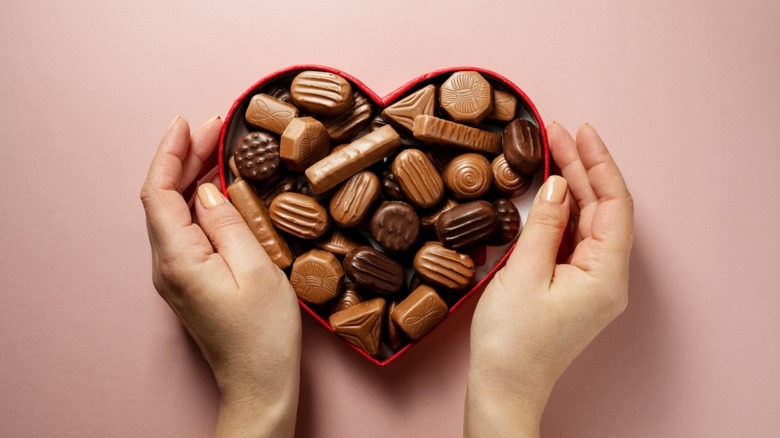 Hands holding a heart-shaped box of chocolates