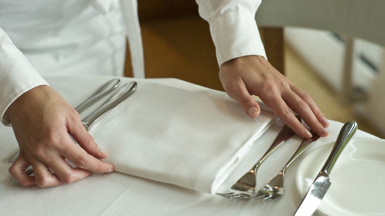 An individual straightening a napkin and silverware at a restaurant table