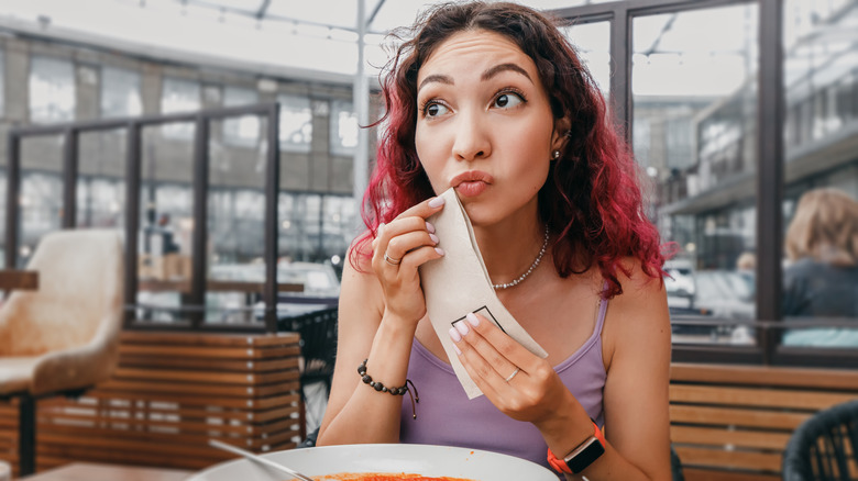 A woman dabbing her face with a napkin while eating