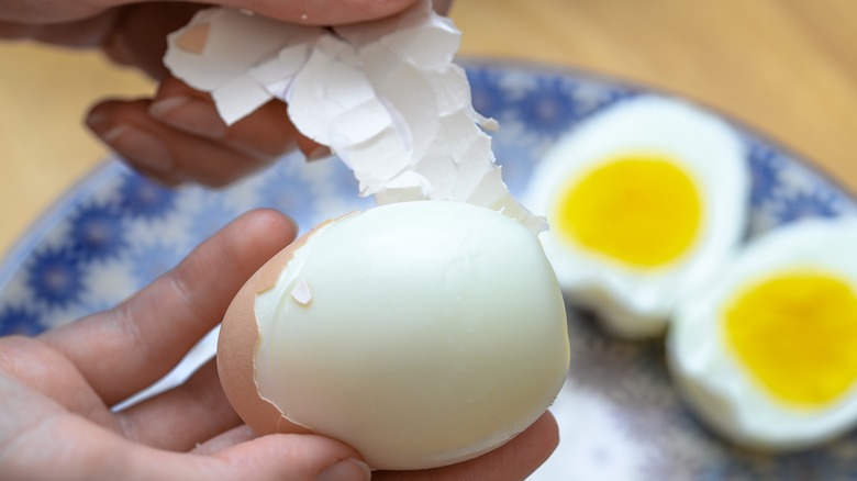 Person's hand holding and peeling a hard boiled egg.