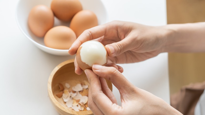 Two hands peeling multiple hard boiled eggs