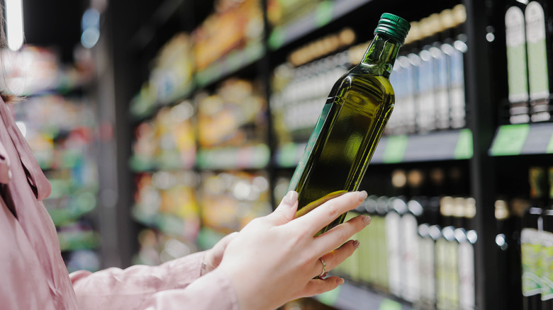 Woman choosing a bottle of olive oil at the grocery store.