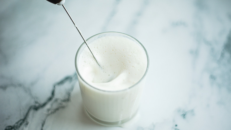 Milk being frothed in a clear glass on the counter.