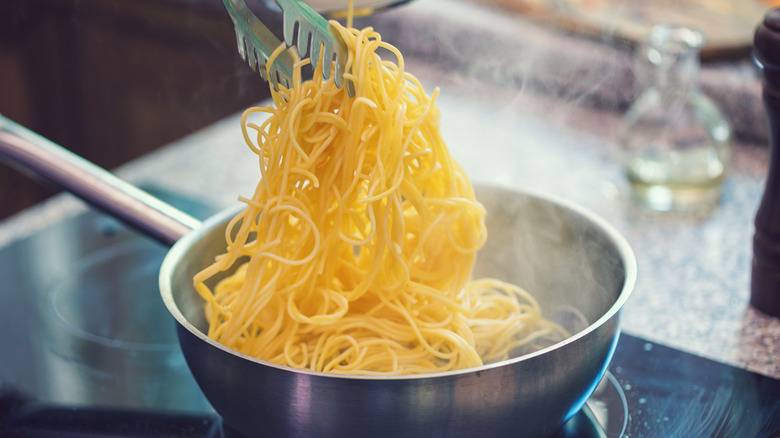 Pasta being picked up out of a pot using tongs